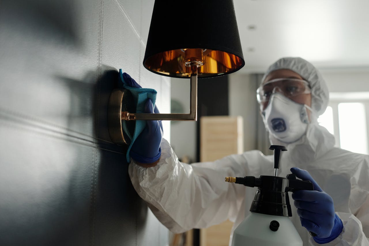 services-04 A person wearing protective gear sanitizes a wall lamp to prevent virus spread.