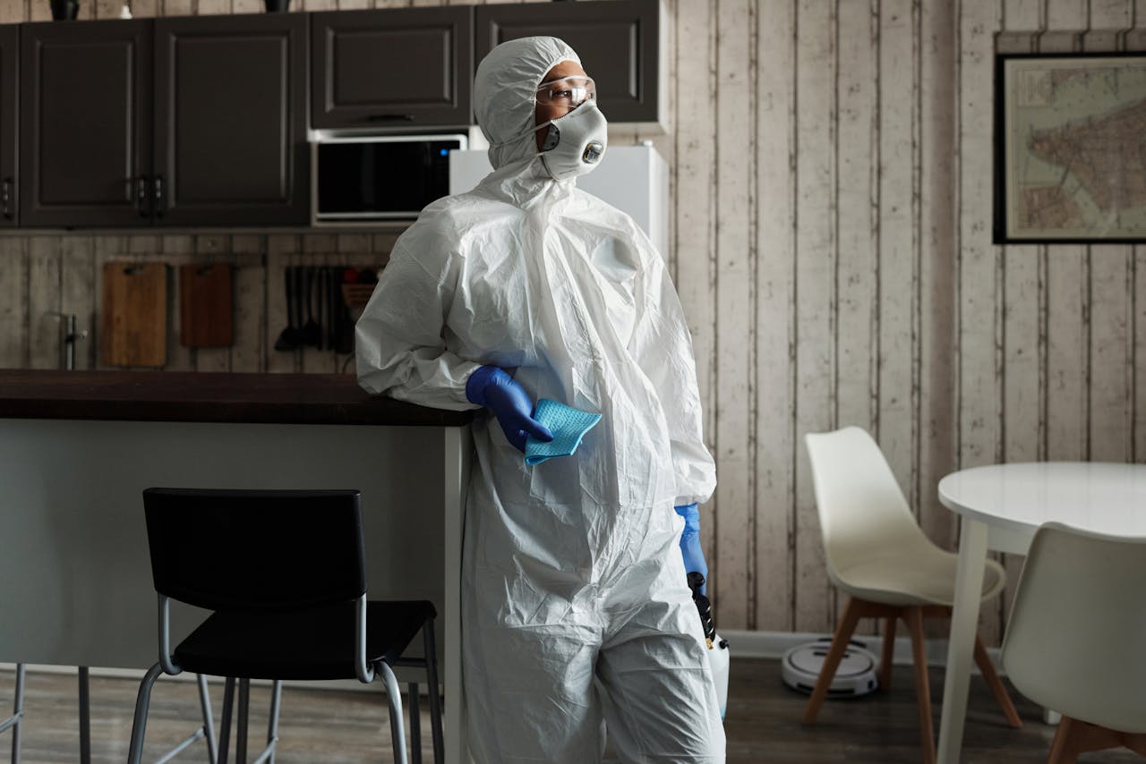 about-01 A person in full PPE gear standing indoors, emphasizing disinfection during COVID-19.